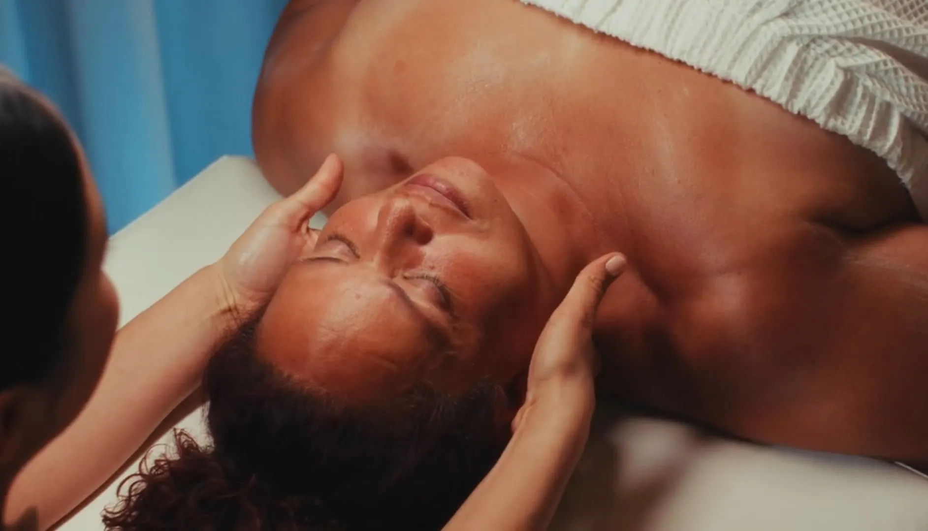 Facial massage with blue curtains behind, hands along the jaw