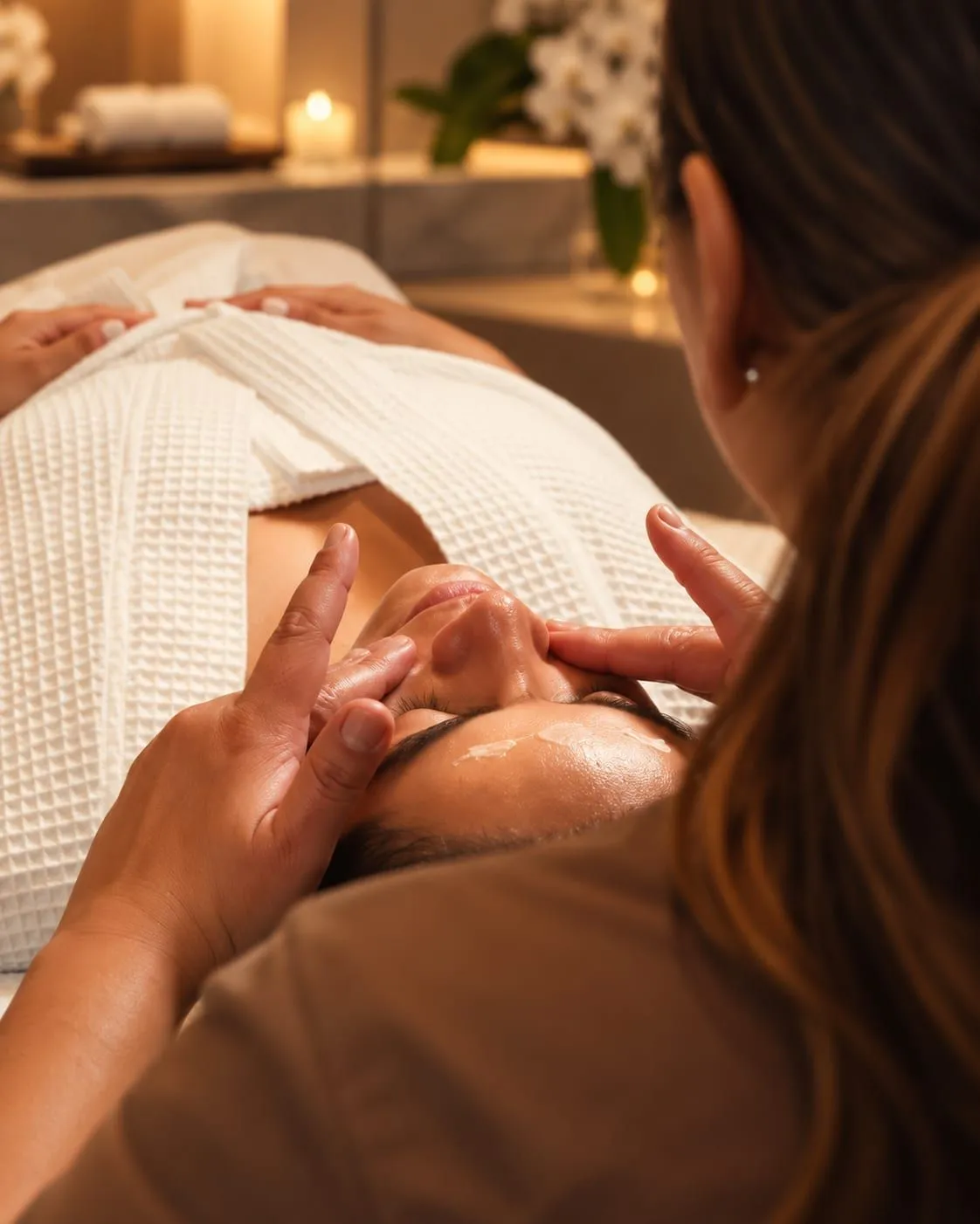 Two therapists apply cream to a guest’s face, seen from behind