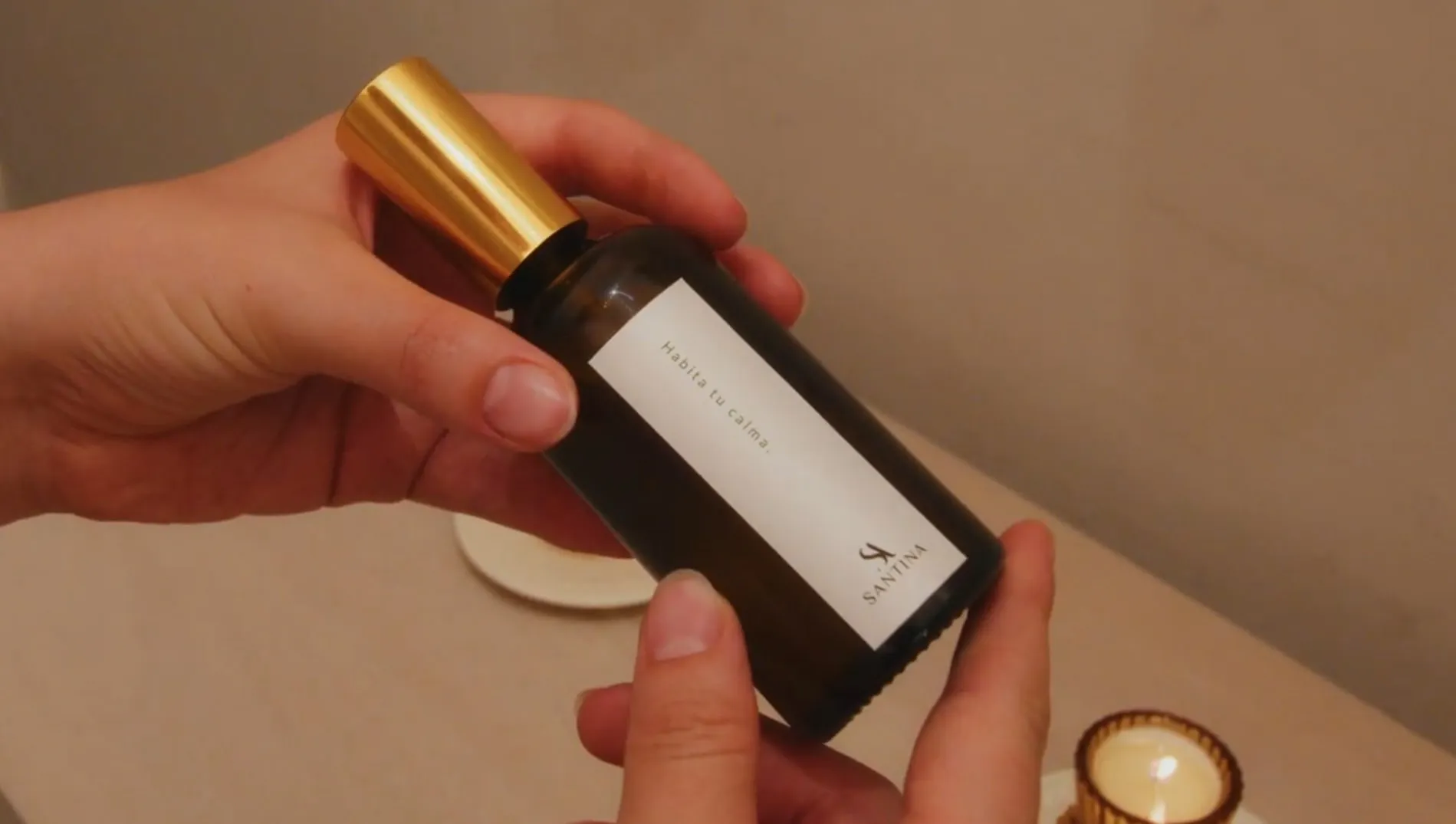 Hands hold the Santina roll-on with its gold cap, a candle lit beside